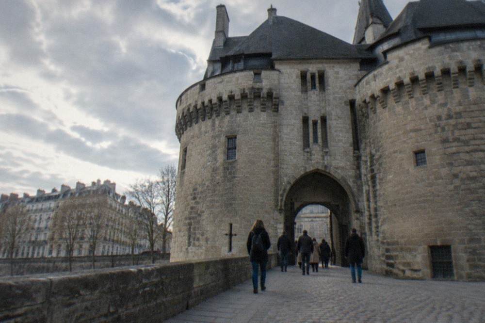 Visitors walking through the arched gateway of a medieval granite fortress in Nantes on a sunny day