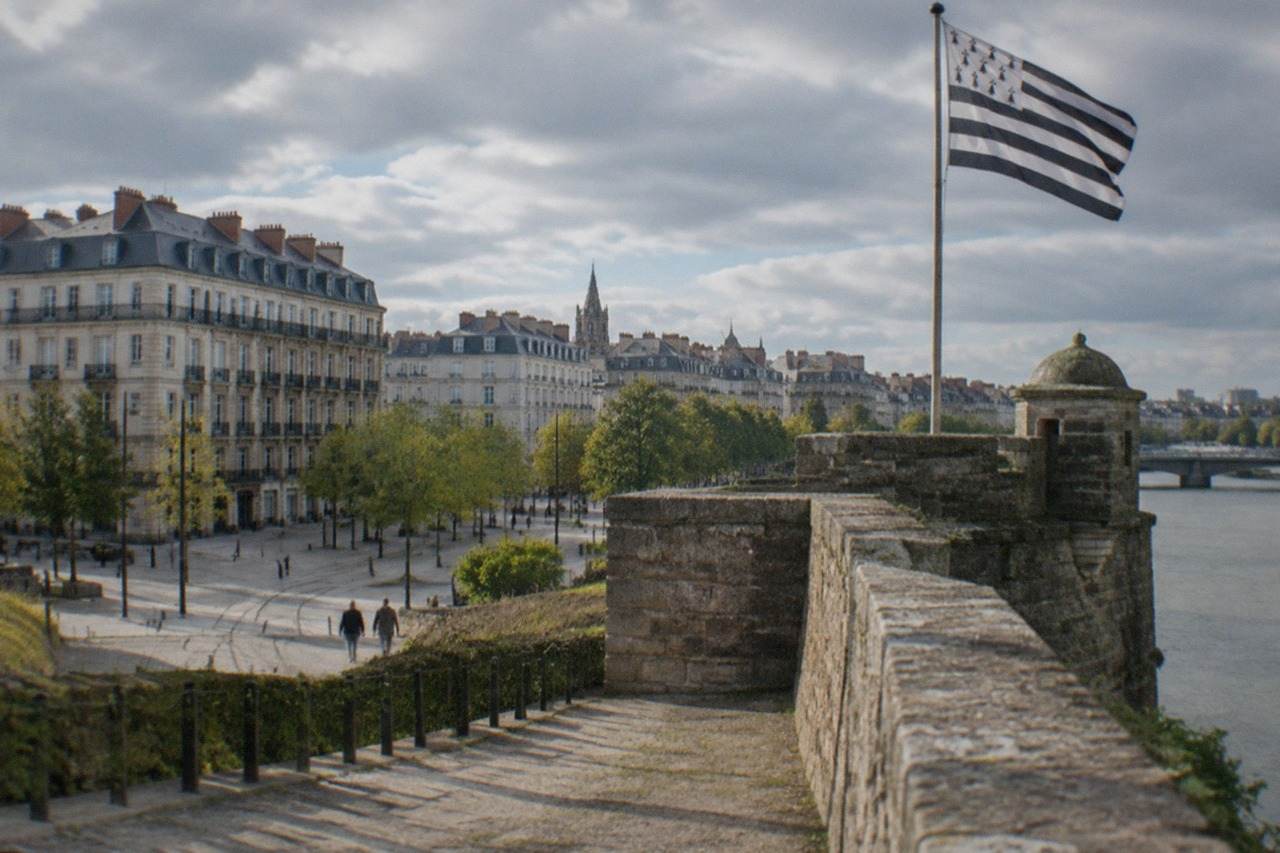 A Breton flag waving beside the ramparts of a historic French city square on a bright day