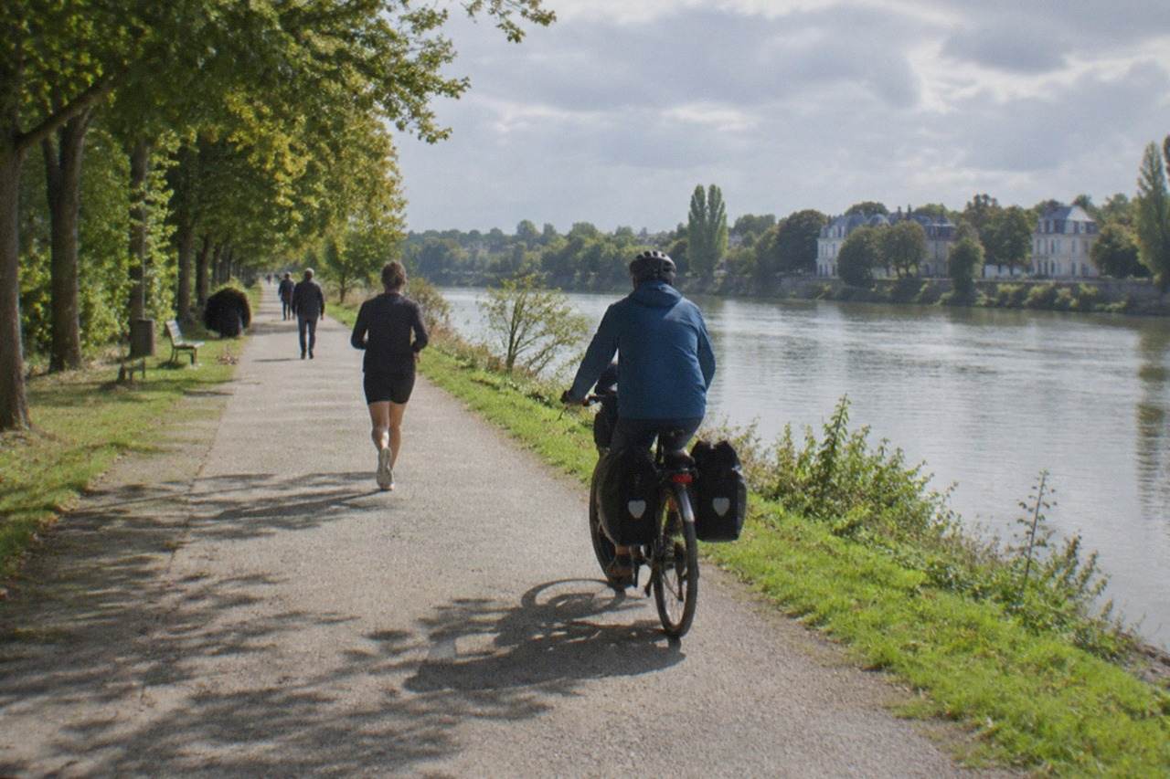 A cyclist riding a touring bike along a riverside path beside the wide Loire, with trees and calm water on both sides