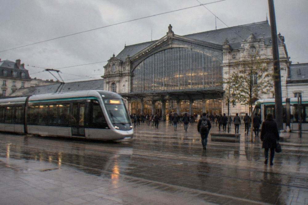 Trams passing outside the entrance of Nantes railway station on a bright afternoon