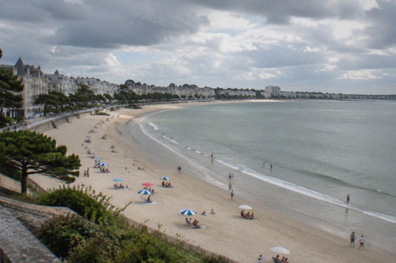 A wide sandy beach curving around a bay with parasols and a calm sea under a summer sky