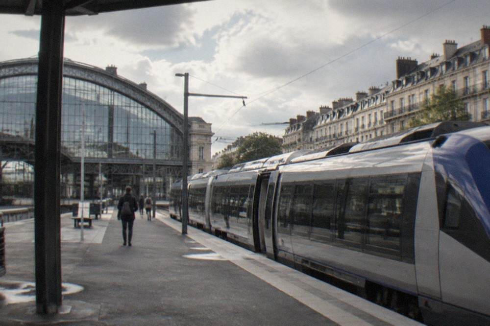 A regional train standing at a platform in Nantes station beside a large glass facade