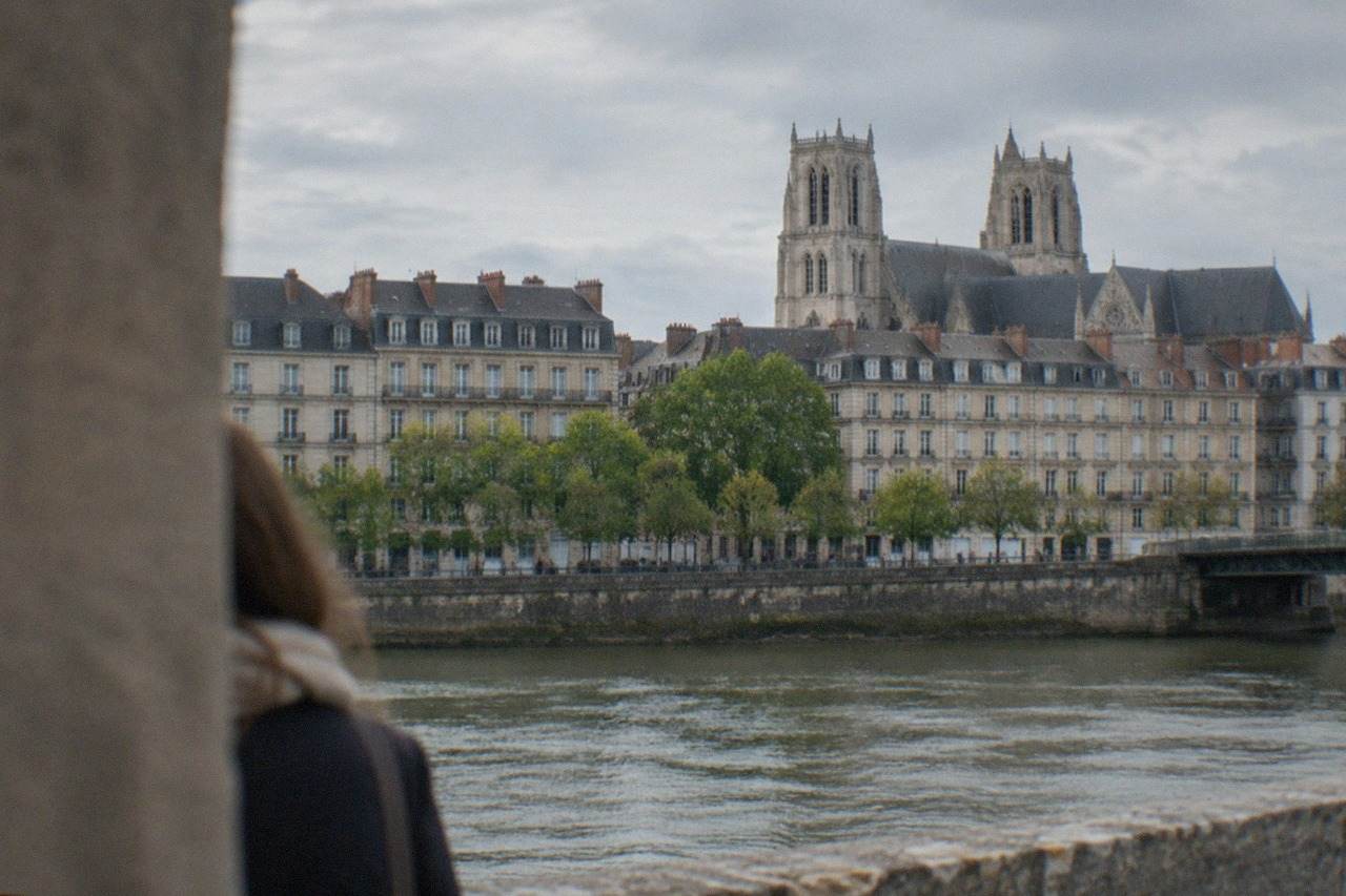 Historic stone buildings of central Nantes seen from across the river, with the cathedral towers rising above tiled rooftops