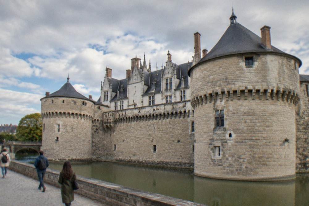 Visitors walking past the stone walls and towers of the Chateau des Ducs de Bretagne on a bright day