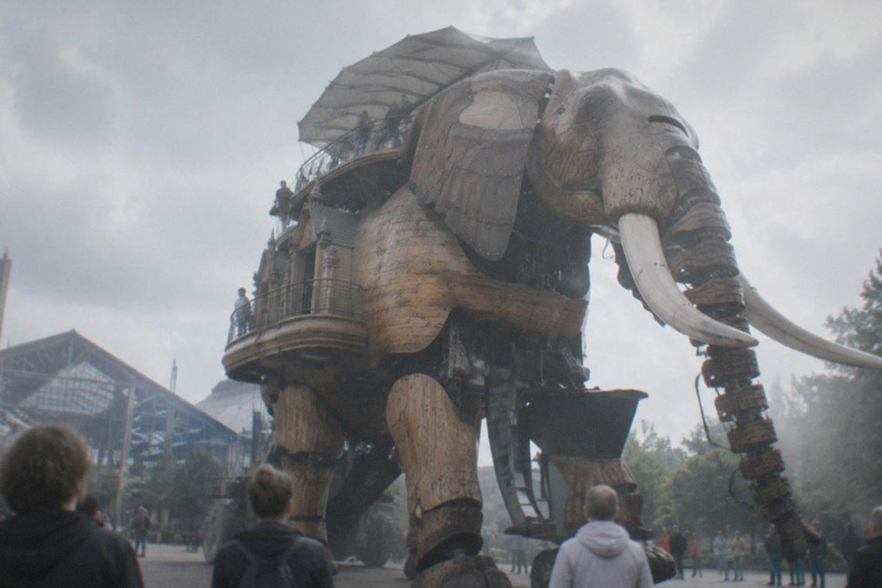 A giant mechanical elephant with wooden legs walking past visitors on a former shipyard site