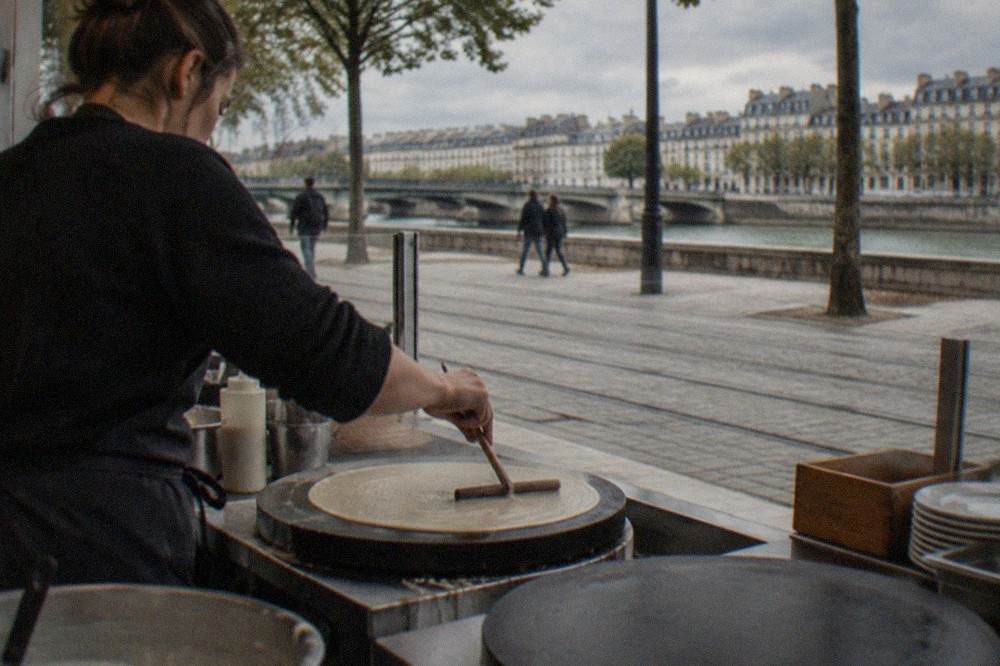 A cook in a Nantes crêperie spreading buckwheat batter on a large round griddle with a wooden spreader