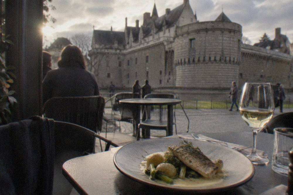 A plate of fresh fish with beurre blanc sauce beside a glass of white wine on a restaurant table