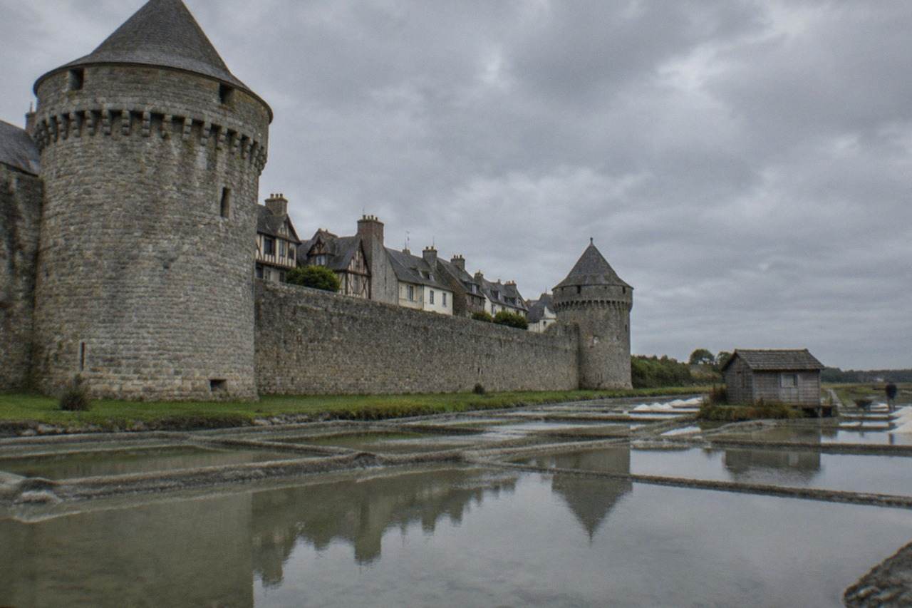 Shallow Guérande salt pans reflecting a pale sky, with a wooden salt worker's hut at the water's edge
