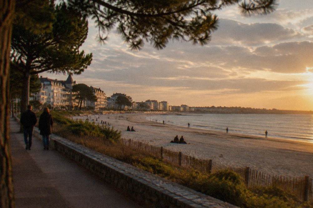 The La Baule seafront promenade at golden hour with apartment buildings and pines behind the sand