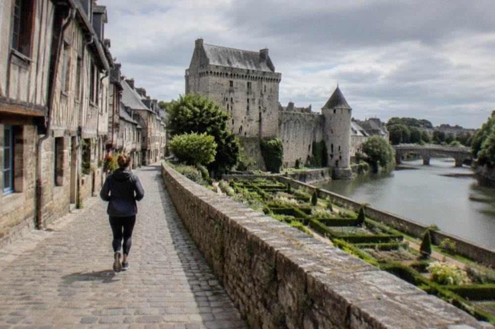 A granite castle keep rising above ramparts beside a small river in a Breton town