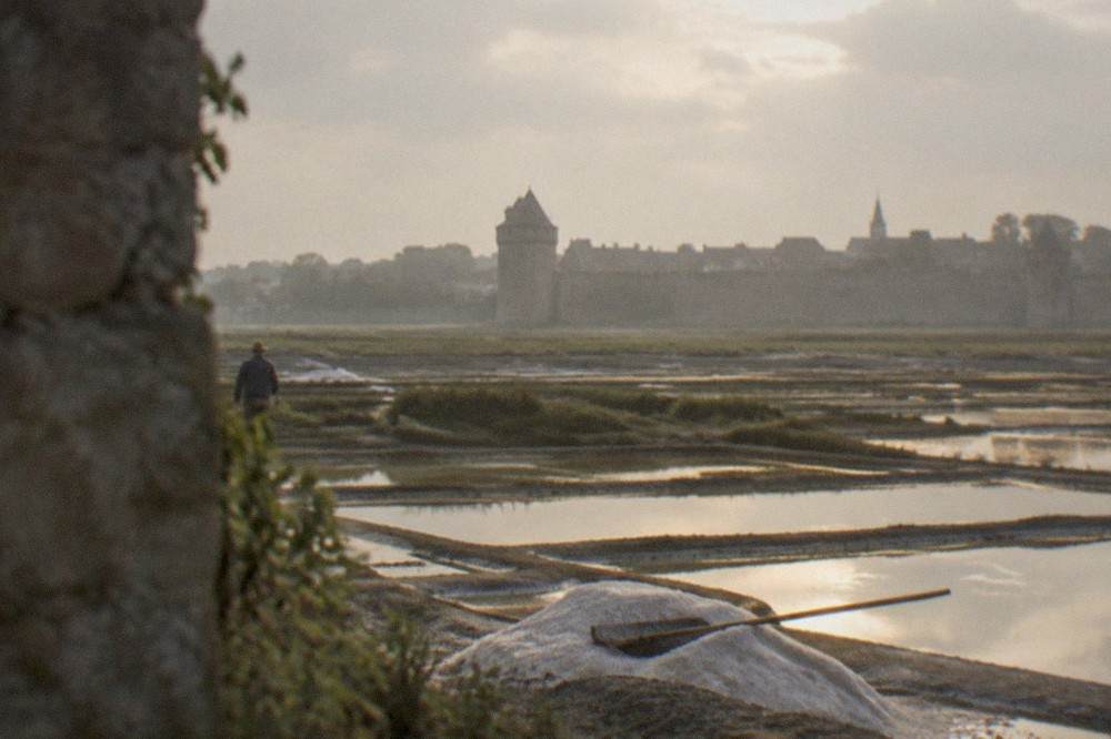 Salt marshes near Guérande at golden hour with a worker's rake resting on a mound of coarse salt