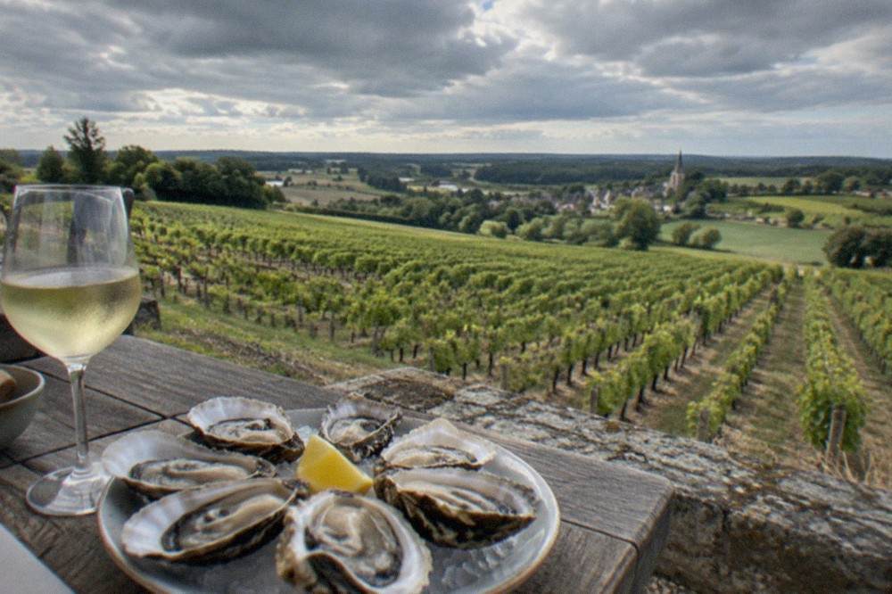 A chilled glass of pale Muscadet white wine beside a plate of fresh oysters on a Nantes restaurant table