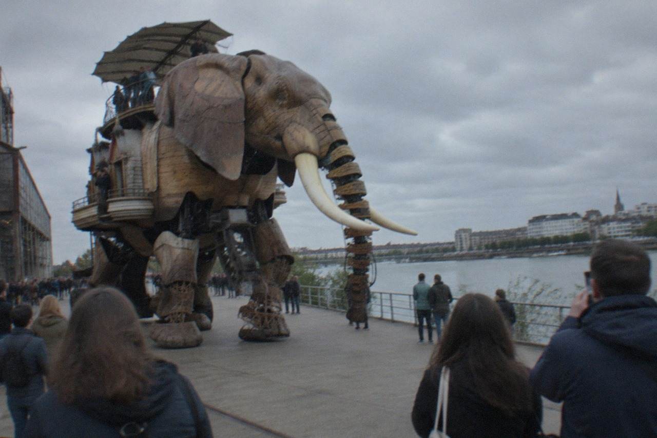 A giant mechanical elephant with wooden lattice legs walking along a waterfront promenade on the Île de Nantes