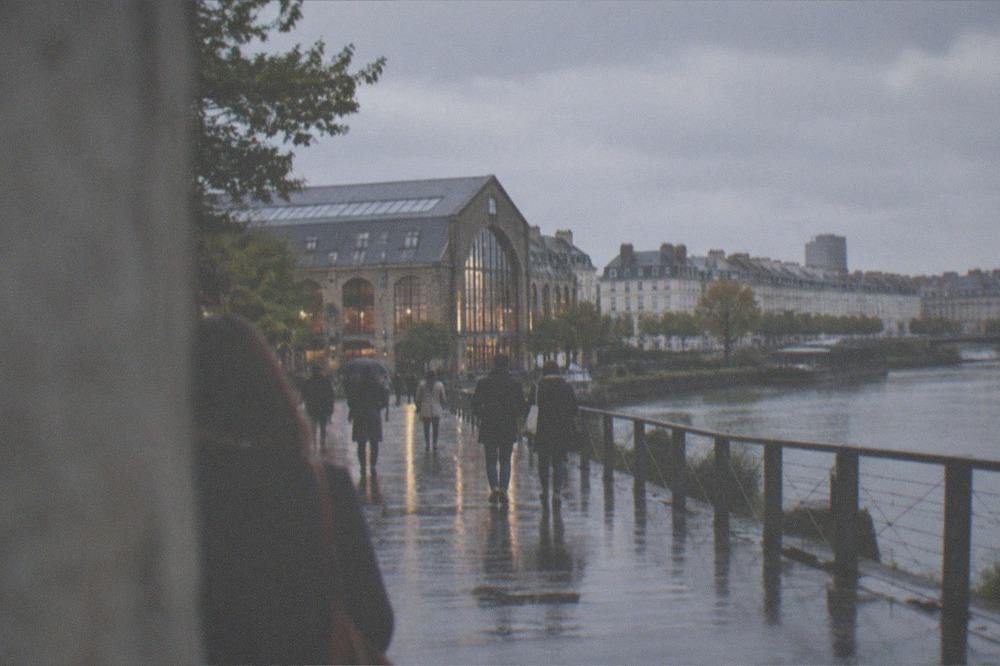 A riverside promenade in Nantes with a converted warehouse building and people walking at dusk