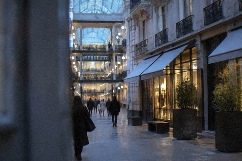 A glass-roofed nineteenth-century shopping gallery with three stacked floors of boutique frontages