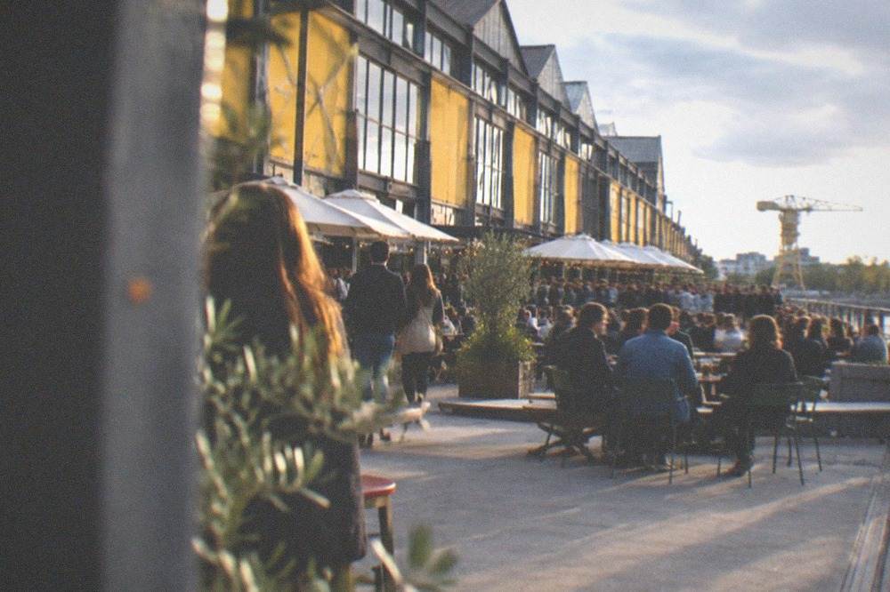 Evening crowds on the terrace in front of the yellow warehouse fronts of the Hangar à Bananes