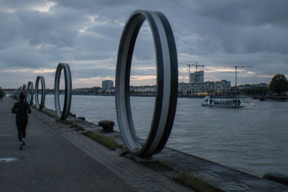 A river shuttle boat crossing the Loire towards a modern island district with cranes and ring sculptures
