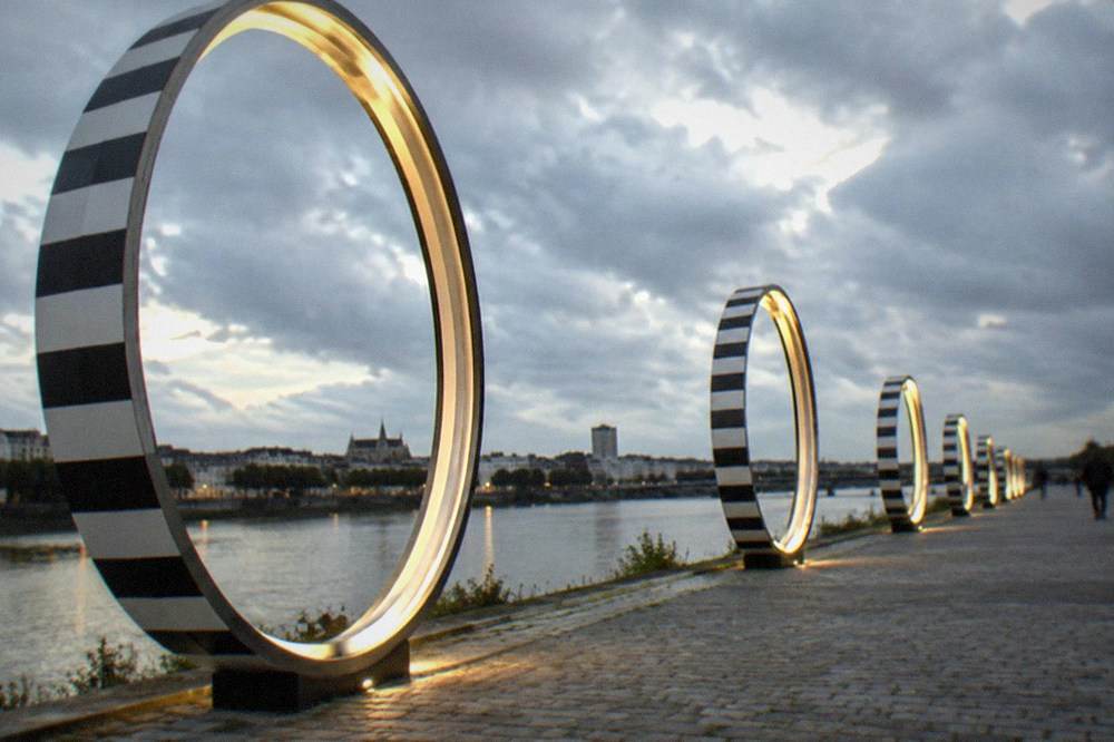 Striped rings glowing under evening lights along a riverside promenade