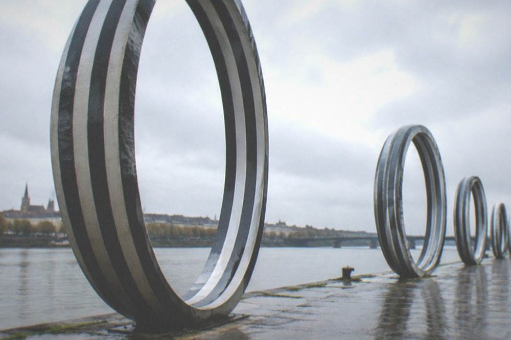 A riverside promenade in soft morning light with ring sculptures and calm water