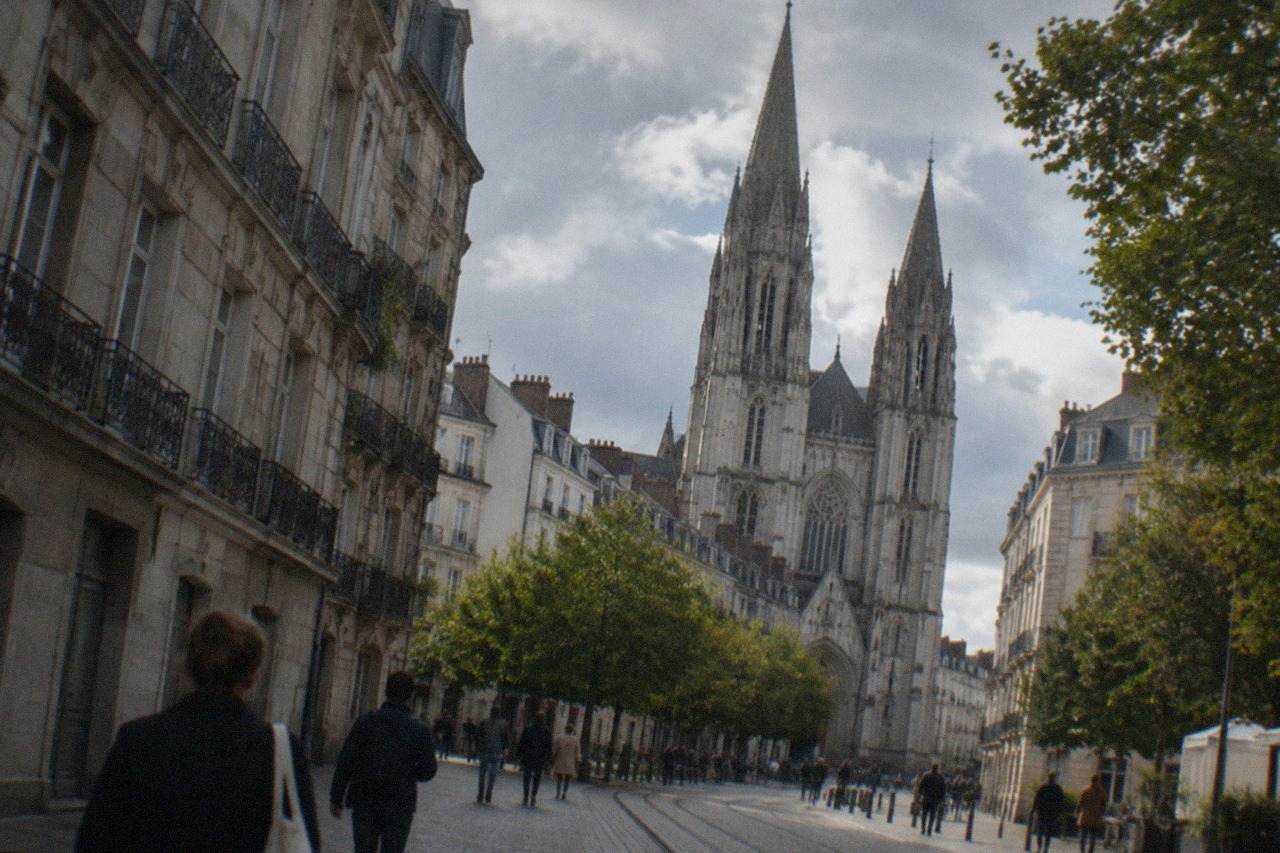 Tall neo-Gothic church towers rising over a narrow street in central Nantes with pedestrians below