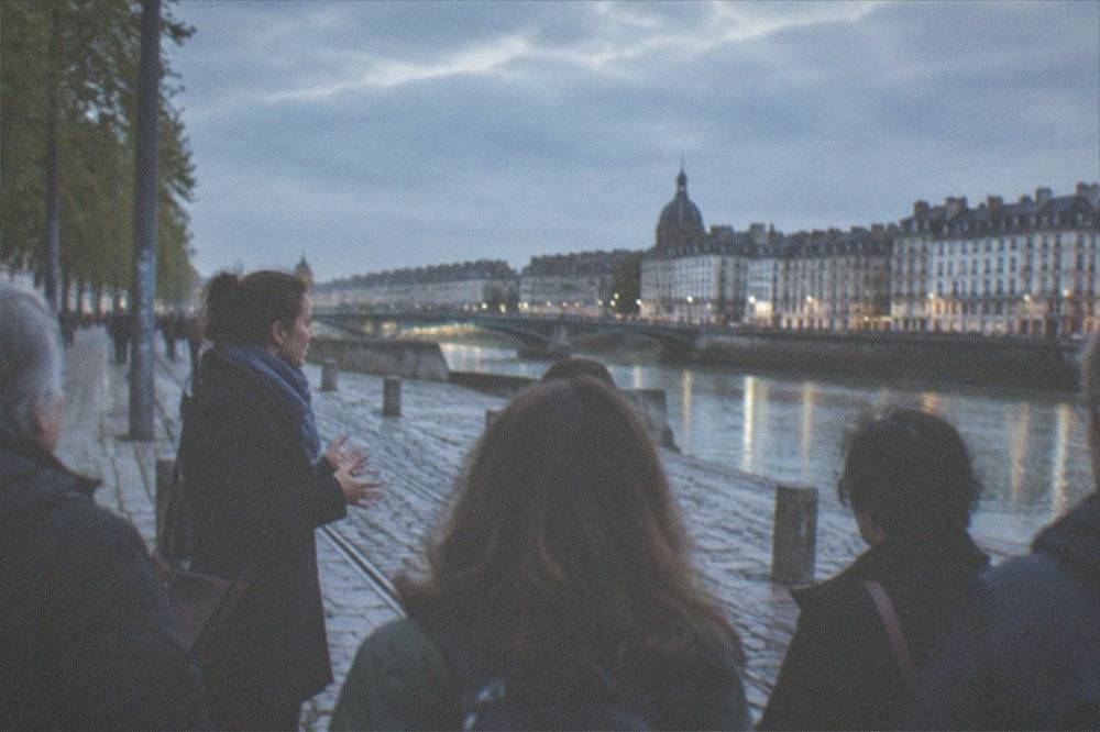 A tour guide speaking to a small group of visitors on a stone street in Nantes