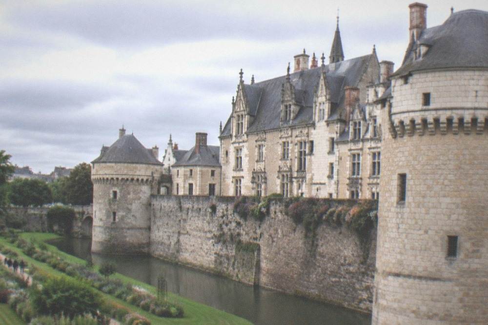 The dry moat garden of the Château des ducs de Bretagne in spring, with green lawns, flower beds and people sitting on benches under the castle walls.
