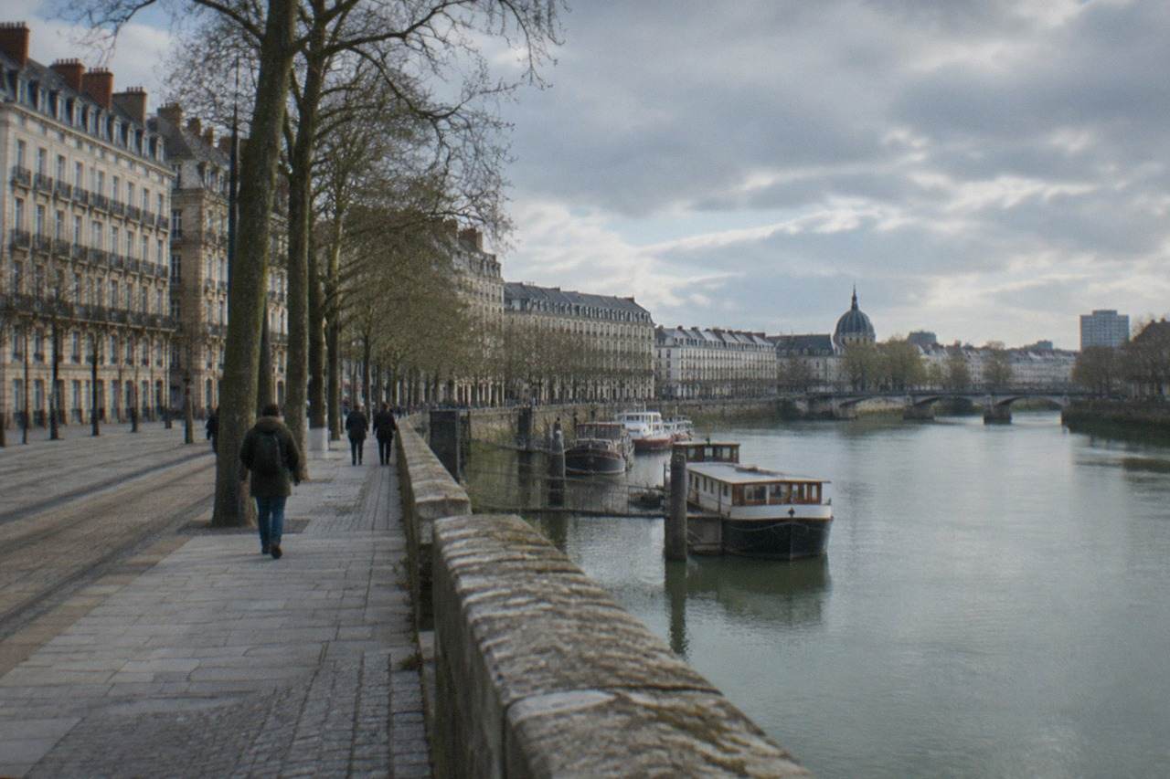 A calm green river flowing past tree-lined banks with moored boats in Nantes, France