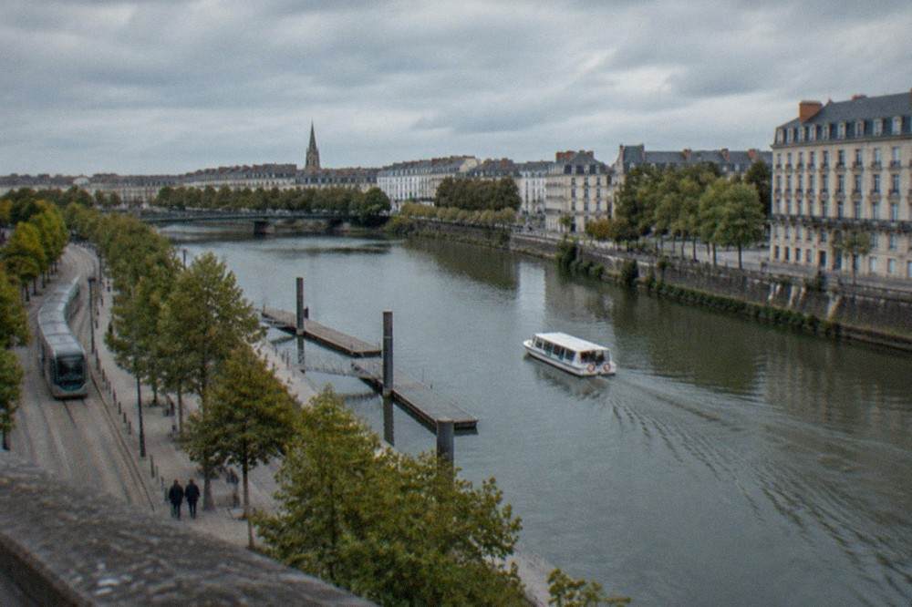 Small white river shuttle boat moving along the Erdre between wooden pontoons