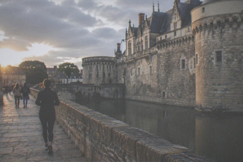 Stone ramparts of a castle courtyard with visitors walking beside a moat in Nantes