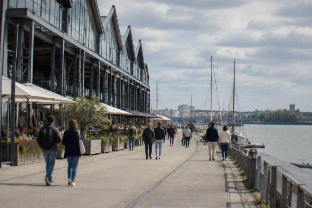 People strolling on the quay in front of the warehouses, with the masts of boats on the Loire behind them