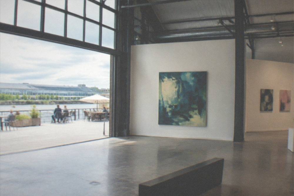 Interior of a bright gallery space inside a converted warehouse, with large contemporary artworks on the walls