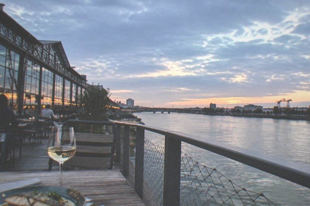 Terrace table with a glass of white wine and a fish dish, overlooking the Loire at sunset