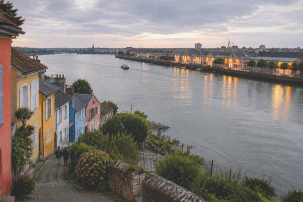 Wide evening view along the Loire, with the lit warehouses of the quay on one bank and Trentemoult's coloured houses on the other