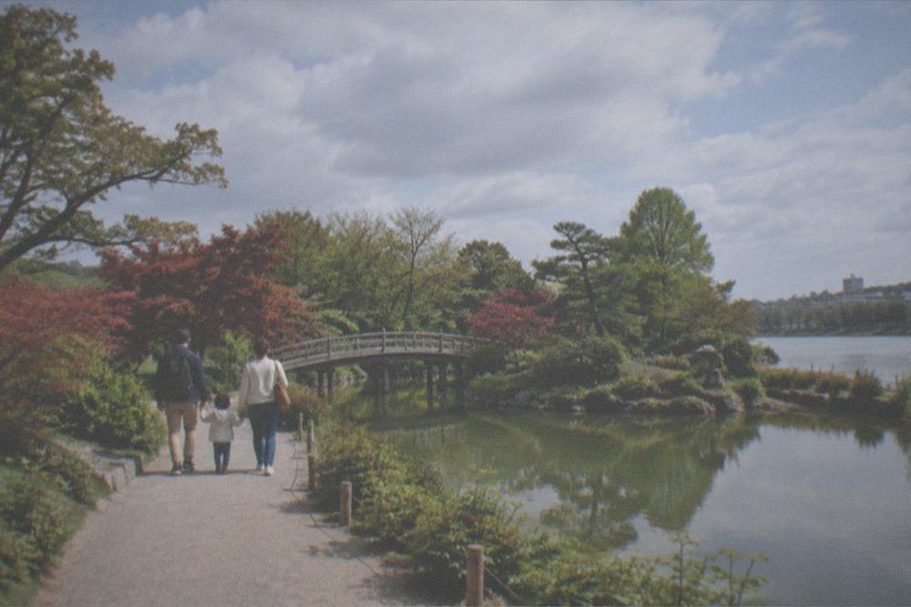 A family strolling a garden path beside a pond on a river island