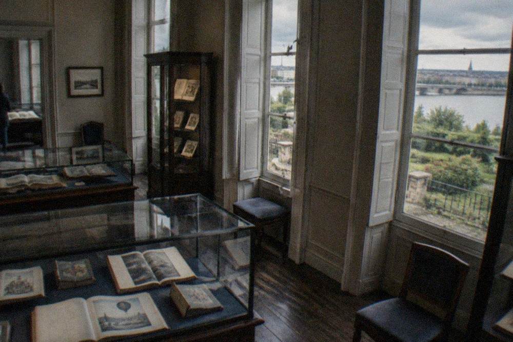 Reading room with glass cases displaying old illustrated books in the Jules Verne Museum in Nantes