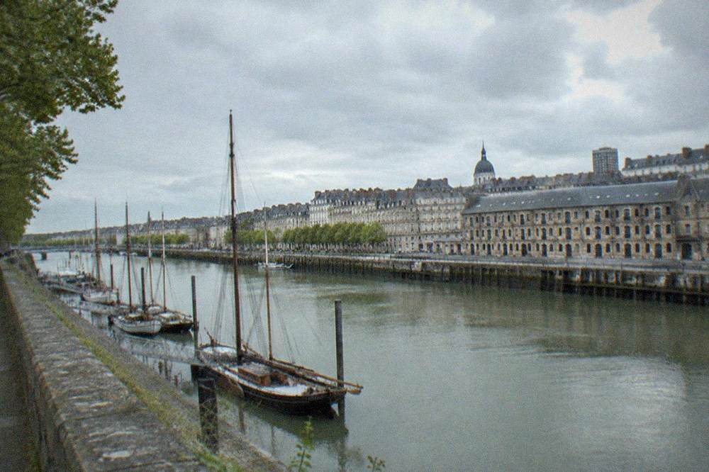 Old port of Nantes seen from a high riverbank, with masts and 19th-century warehouses along the water