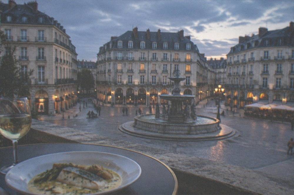 A plate of fish in a creamy butter sauce beside a glass of white wine on a brasserie table