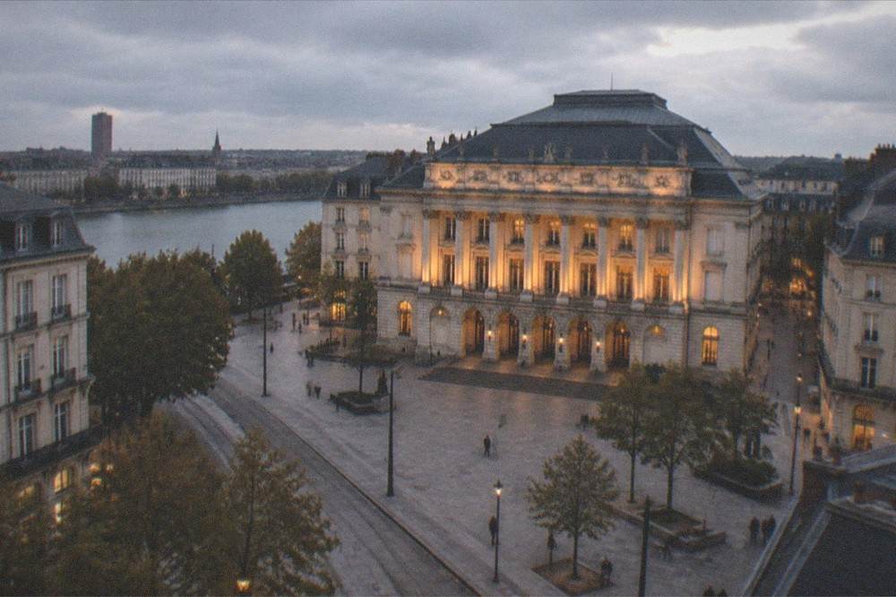 The facade of the Nantes opera house illuminated at dusk above a quiet city square