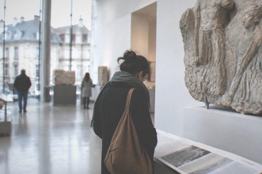 A visitor reading interpretation panels beside a large stone relief fragment in a bright gallery