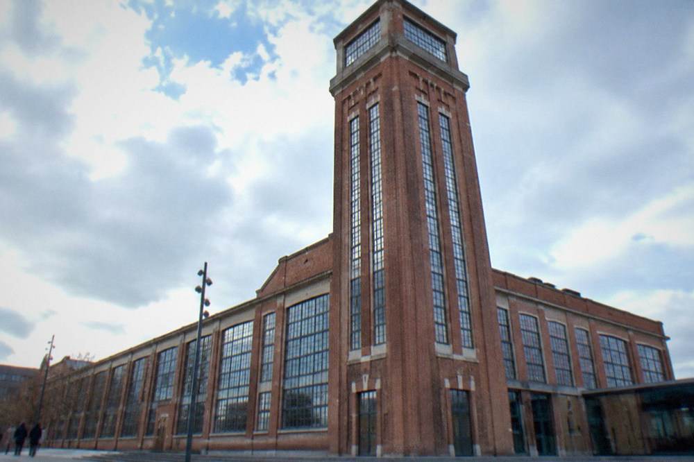 The tall brick tower of the former LU factory seen from below against the sky