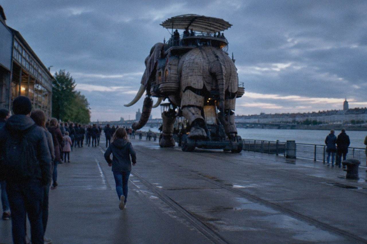 A giant mechanical elephant walking along the riverside quays of the Ile de Nantes with visitors watching from the side