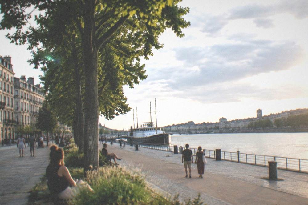 Summer sunshine on the Loire riverfront in Nantes with trees, a wide quay and a ship moored in the distance