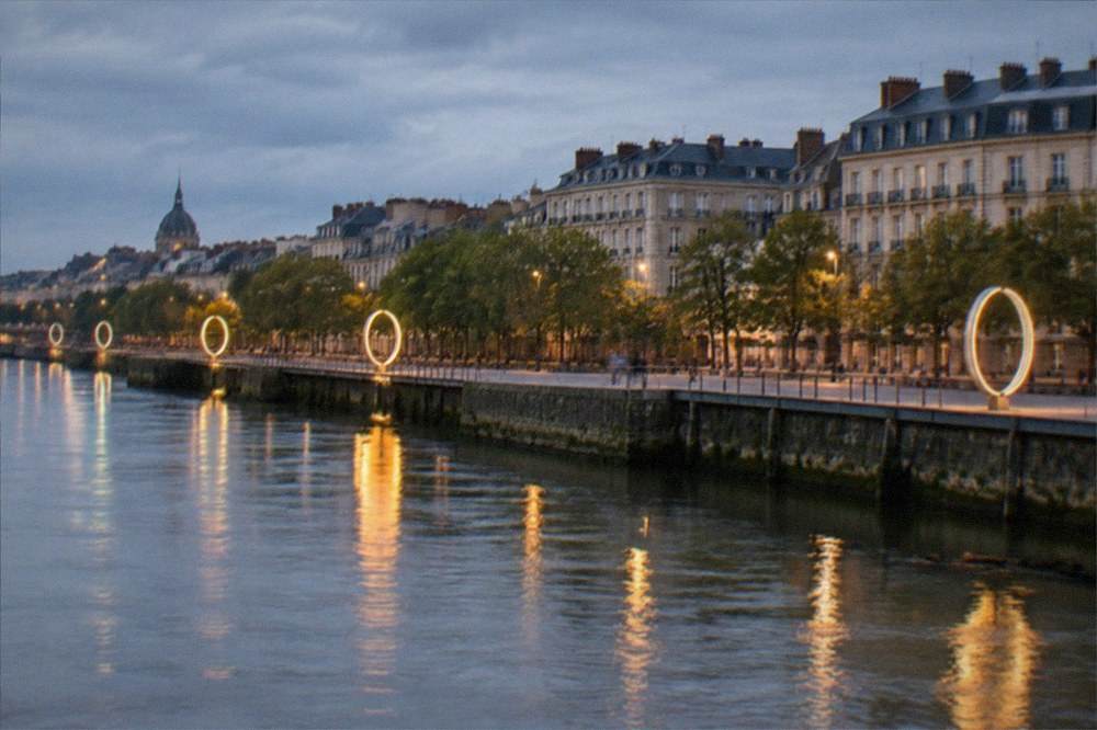 Evening lights on the Loire in Nantes with illuminated rings standing along the quay and reflections on the water