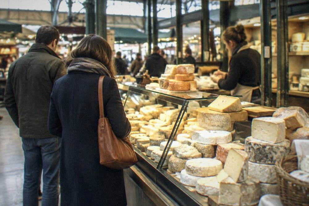 Shoppers browsing a cheese stall in a covered market hall in Nantes