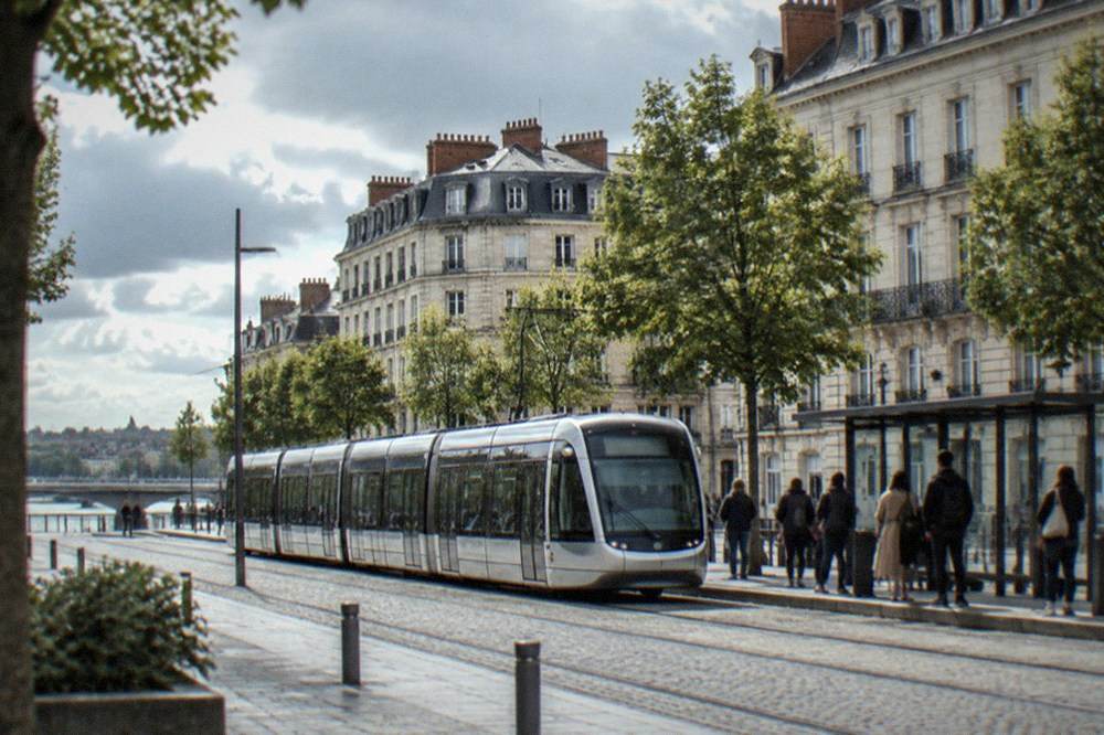 A tram passing along a central Nantes street with passengers waiting at a sheltered stop