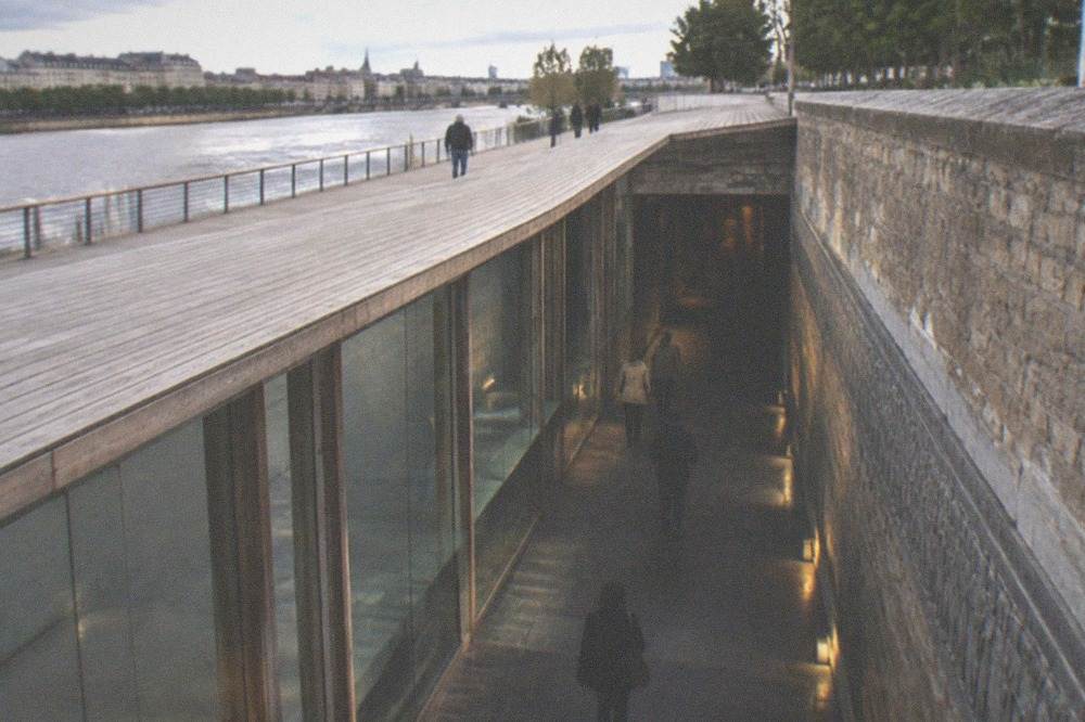 The low stone-walled underground corridor of the memorial with dim lighting and text carved along the wall
