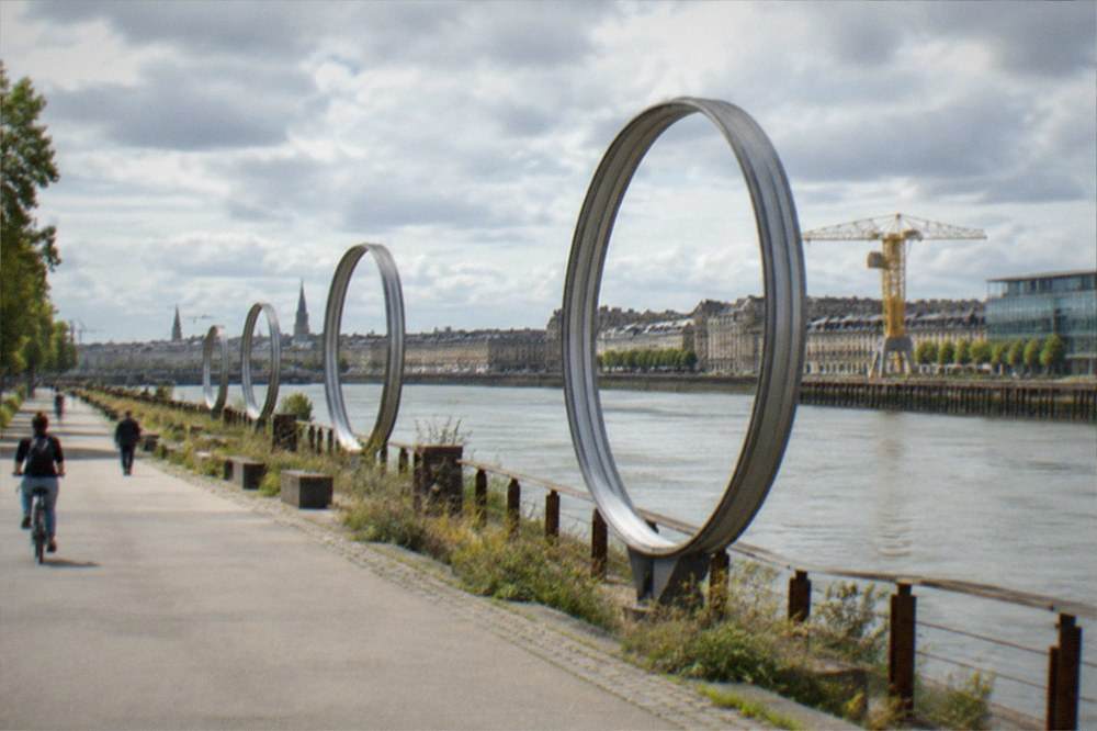 Tall metal rings standing along the quay of the Île de Nantes with the river and city buildings behind