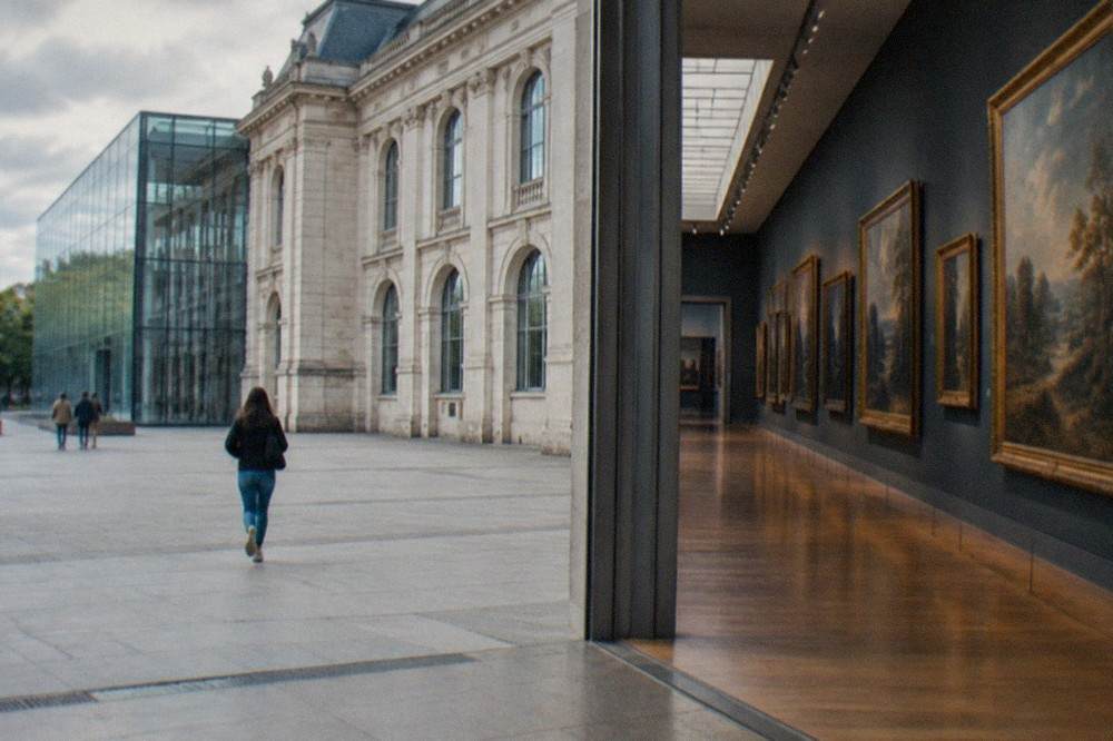 Sunlit gallery hall with classical oil paintings hung frame to frame on deep walls