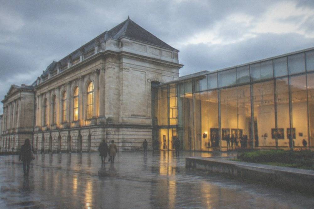 Evening view of a museum gallery with warm lighting and a few visitors browsing