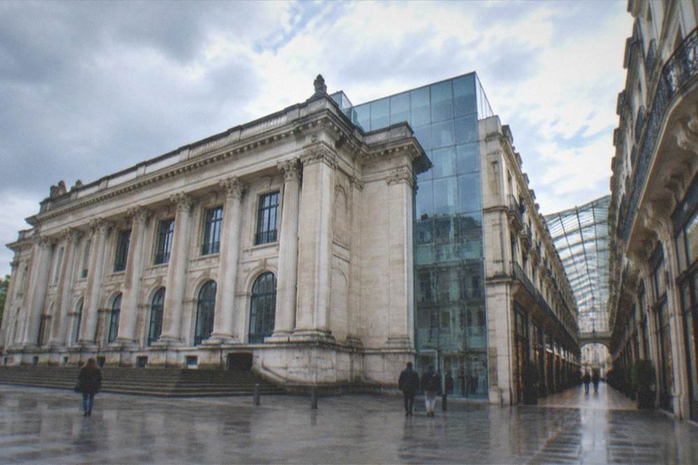 Narrow shopping arcade with glass roof and elegant balconies above boutique storefronts